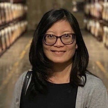 Une femme à lunettes et aux cheveux noirs sourit à la caméra.